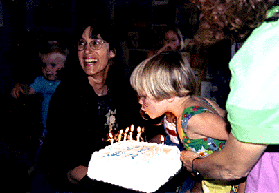 [Photo of child blowing out Children's Center birthday cake candle, with Lise Bixler]
