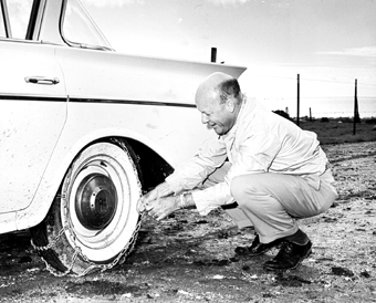 [Photo of Dean McHenry putting chains on a car's tire]