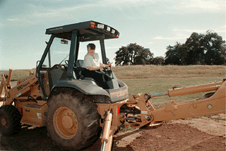 [Photo of Chancellor Greenwood, working the controls of a back hoe at the site of the new Fitness Center]